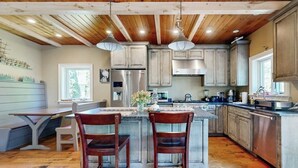 A kitchen with wooden ceiling beams, a central island with two chairs, stainless steel appliances, and light-colored cabinetry. - Dog-friendly Home With High-speed Wifi, Washer/dryer, & Private Dock (Harpswell)
