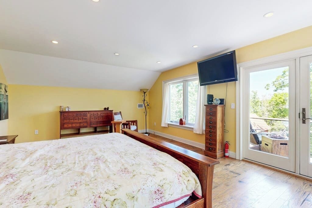 Een slaapkamer met een bed, een houten dressoir, een televisie en een openslaande deur naar een balkon.
