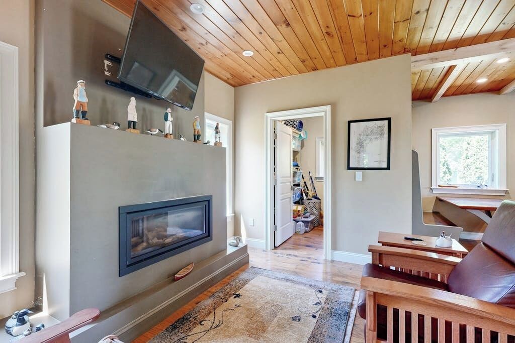 A living room with a fireplace, wooden ceiling, and a TV mounted above it.