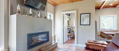 A living room with a fireplace, wooden ceiling, and a TV mounted above it.