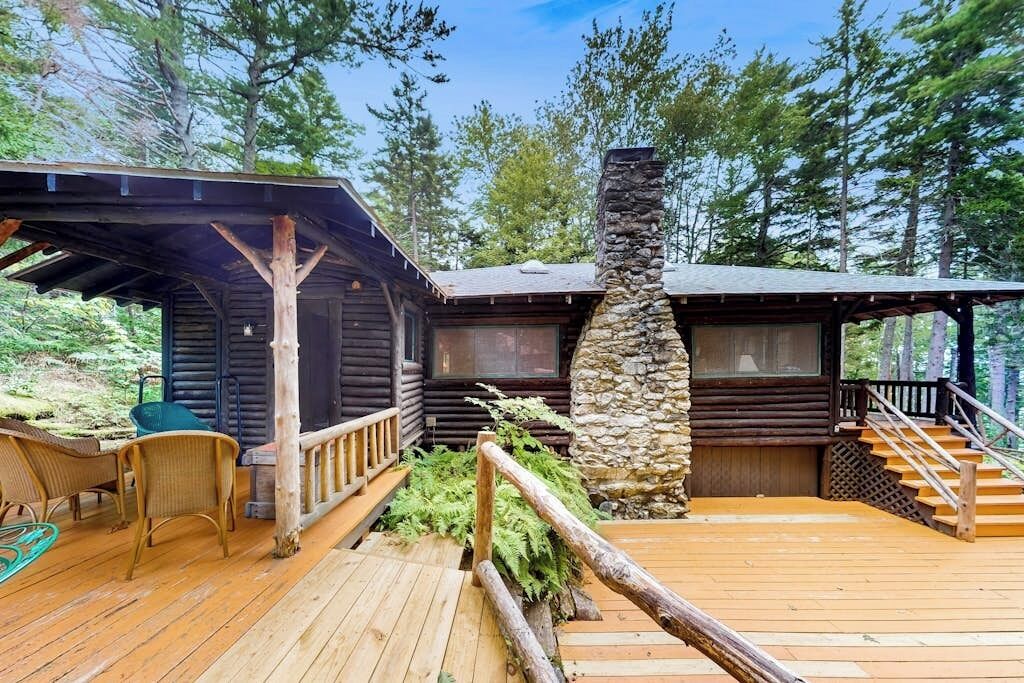 A cabin with a wooden deck, stone chimney, and a covered porch area.