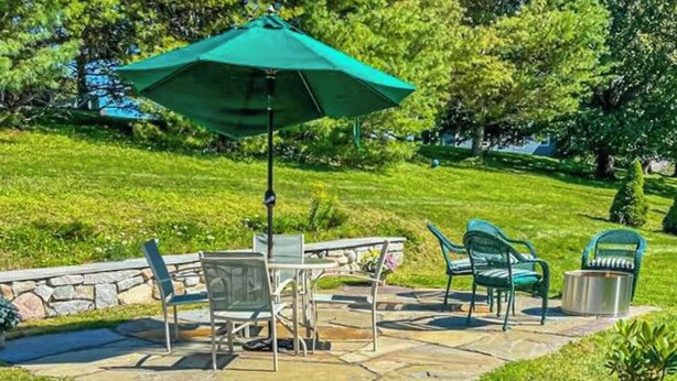 A patio with stone flooring, outdoor furniture, and a green umbrella. - Charming Coastal House With Cozy Living Spaces and Outdoor Firepit (Winter Harbor)