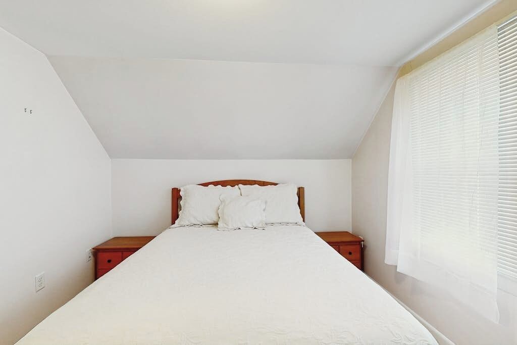 A bedroom with a bed, two nightstands, a wooden headboard, and a window with blinds.