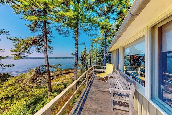 A wooden deck with a bench and a chair overlooking a body of water, surrounded by trees. - Beachfront Delight With Detached Guesthouse, Private Beach Access, Dog-friendly (Southport)
