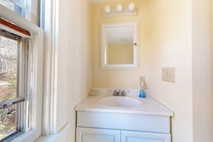 Un baño con un lavamanos blanco, un espejo y una ventana.