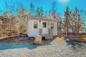A small, single-story cabin with a front porch, surrounded by trees. - Charming Love Shack With Stunning Seaside Views and all the Comforts of Home (Trenton)