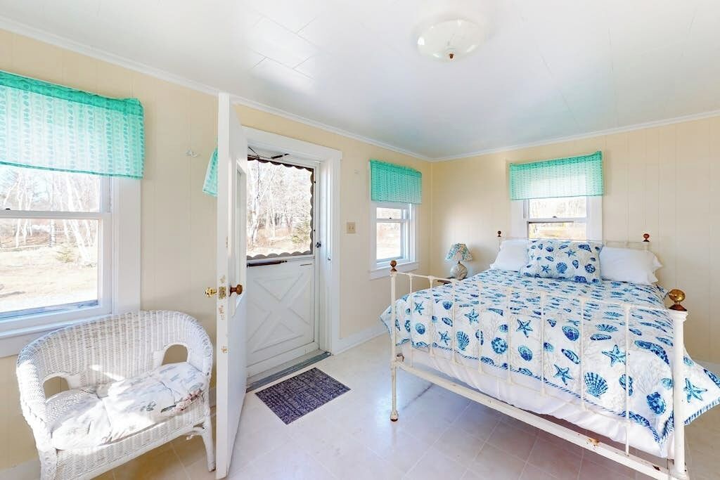 A bedroom with a bed, a chair, a door, and windows with curtains.