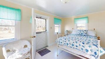 A bedroom with a bed, a chair, a door, and windows with curtains.