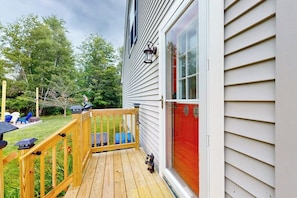 A wooden deck with a railing, a red door, and a window with a light fixture. - Serene Home With a Deck, Grill, Firepit, Board Games, Washer/dryer, & mtn Views (Ellsworth)