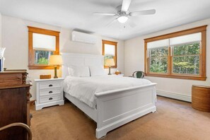A bedroom with a white bed, wooden headboard, two bedside tables with lamps, a ceiling fan, and large windows. - Hillhouse, Tastefully Decorated Maine Home (Rockport)