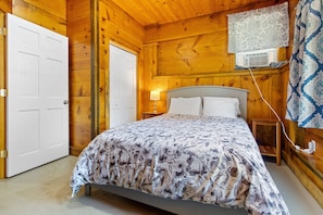A wooden room with a bed, a door, and a window with a patterned curtain. - Cozy Lakefront Cottage With Stunning Views, Deck, BBQ Grill, and Outdoor Firepit (Newcastle)