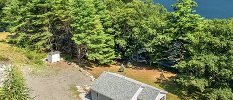 A cabin with a gravel driveway, surrounded by dense forest and a lake.