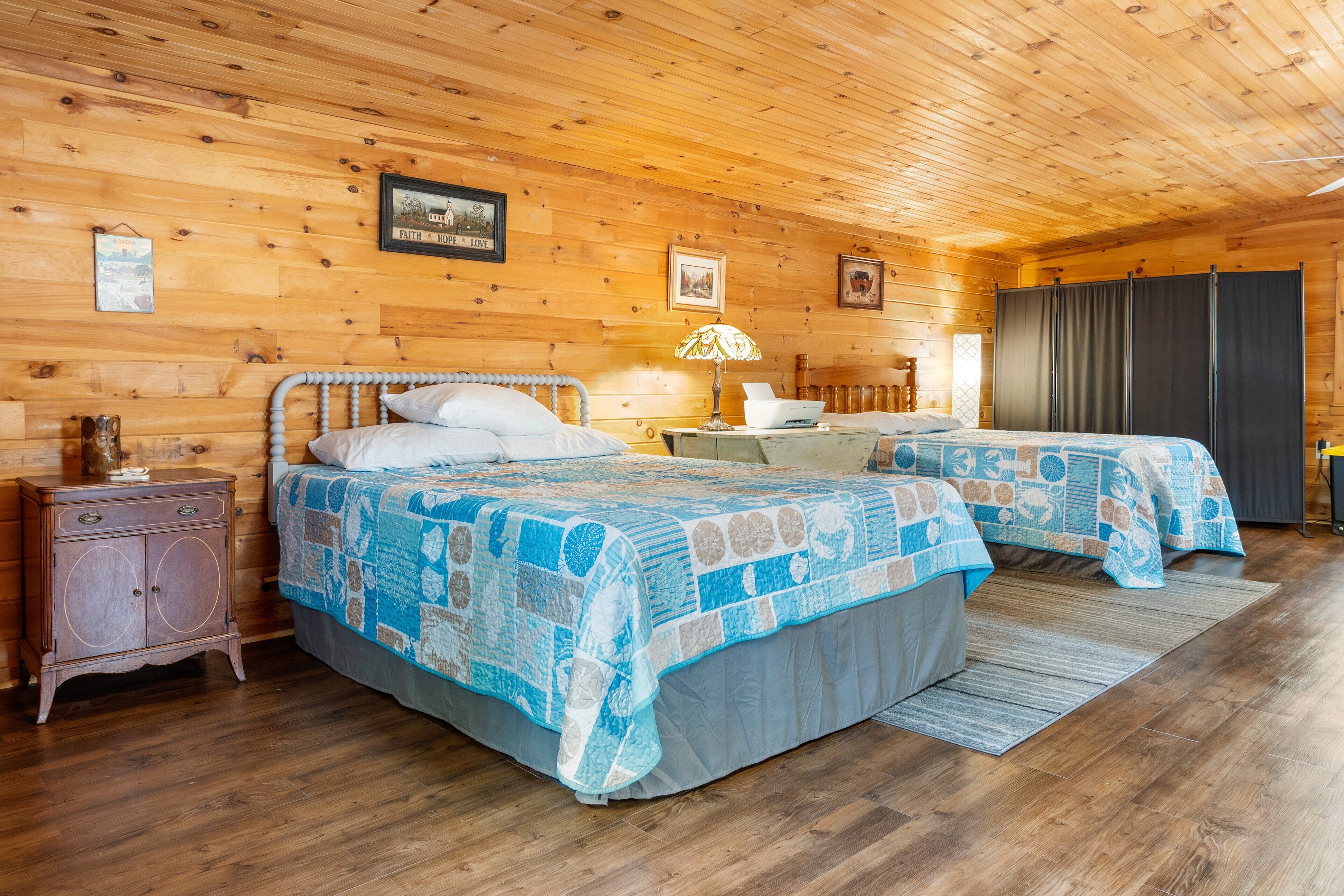 Quarto estilo cabana de madeira com duas camas, uma mesa de cabeceira, um penteado e uma luminária.