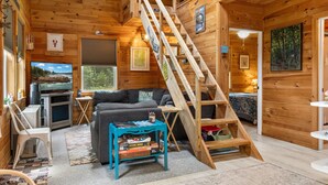 A cabin interior with a wooden staircase, a sofa, a coffee table, and a television. - Waterfront Home on Graham Lake With Kayaks, Bikes, Firepit & Fireplace (Ellsworth)