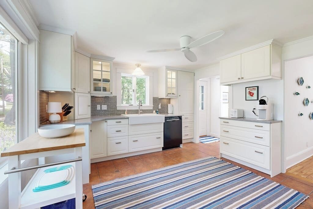 Une cuisine moderne avec des meubles blancs, un îlot central et un tapis à rayures.