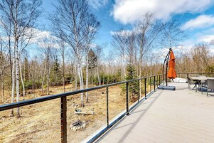 Um terraço com guarda-corpo, móveis de exterior e vista para uma área arborizada.