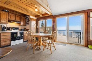 A kitchen with wooden cabinets and a dining area with a table and chairs. - Little White Caps, Quaint Maine Cottage (Tenants Harbor)