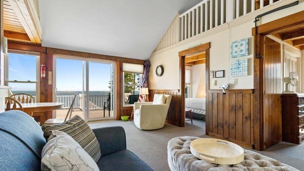 A cozy living room with a sofa, ottoman, and a dining area with a table and chairs. - Little White Caps, Quaint Maine Cottage (Tenants Harbor)