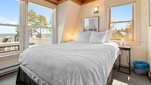 A bedroom with a bed, two windows, a painting, a nightstand, and a view of the outdoors. - Little White Caps, Quaint Maine Cottage (Tenants Harbor)