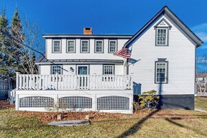 A two-story white house with a balcony, a small porch, and a flag.