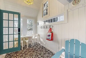 A room with a patterned floor, a white door, a table with chairs, a wall-mounted shelf, and a clock.