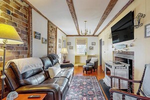 A living room with a leather sofa, a fireplace, a television, and a chandelier.