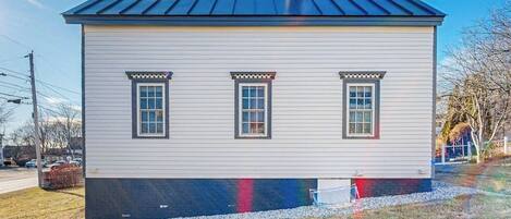 A small, single-story house with a dark roof, three windows with decorative trim, and a chimney.