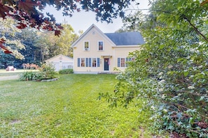 A two-story house with a front lawn, a small garden, and a garage. - Renovated 19th-century Farmhouse w/ 270 Feet of Waterfront & Sunset Views (Penobscot)