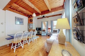 A cozy living area with a wooden ceiling, a dining table with chairs, a sofa, a TV, and a lamp. - Home With Deck, Great Location in the Heart of Acadia National Park (Mount Desert)
