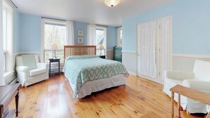 A bedroom with a bed, two chairs, a dresser, and a window with curtains. - Home With Deck, Great Location in the Heart of Acadia National Park (Mount Desert)