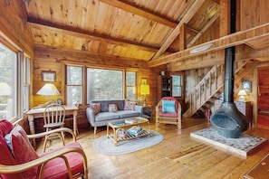 Ein Blockhaus-Interieur mit einer Couch, Sesseln, einem Couchtisch, einem Kamin und einer Treppe.