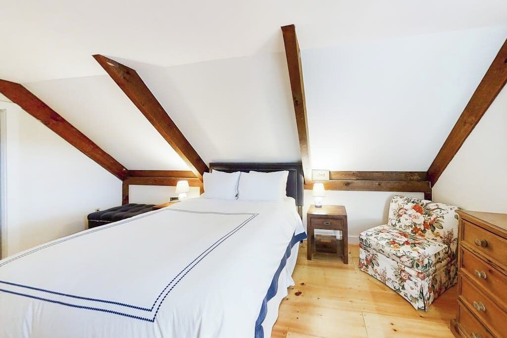A bedroom with a large bed, a nightstand, a chair, and wooden beams on the ceiling.