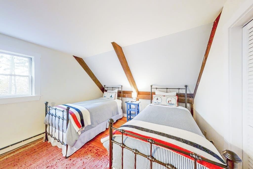 A bedroom with two beds, a window, and a sloped ceiling.