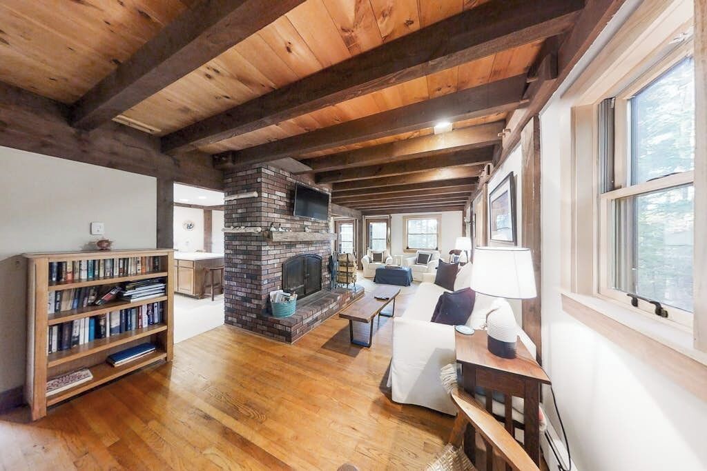 A spacious living room with a fireplace, wooden bookshelves, and a view through large windows.