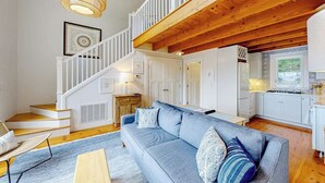 Ein großzügiger Wohnbereich mit blauem Sofa, einer Holztreppe und einer Küchenzeile.
