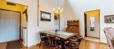 A dining area with a wooden table and chairs, a chandelier, and a mirror above the table.