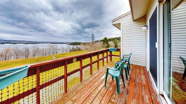 Une terrasse en bois offrant une vue sur un lac et des arbres, avec une rambarde et une porte-fenêtre coulissante.