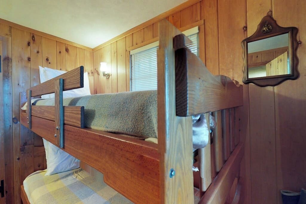 A bunk bed with a headboard, a wall-mounted mirror, and wooden paneling.