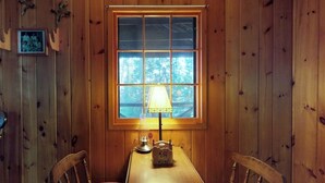 Um quarto com painéis de madeira, uma mesa, cadeiras, uma janela com vista e uma luminária.