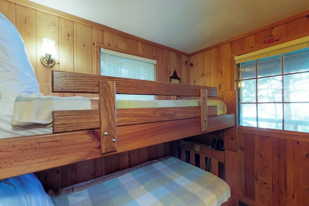Ein Schlafraum mit Etagenbetten, Holzwänden, einem Fenster und einer Wandleuchte.