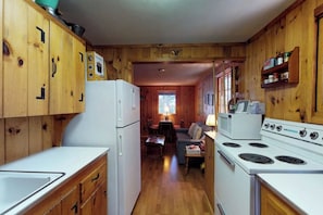 A cabin interior with wooden walls, a kitchenette with a refrigerator and stove, a dining area with a table and chairs, and a window providing natural light. - Lakefront Cabin With Private Dock & Beach Access (Greenville)