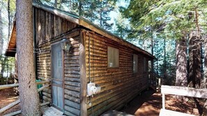 Uma cabana de toras com um alpendre de madeira, uma porta e uma janela.