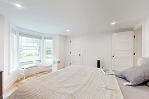 Ein Schlafzimmer mit einem großen Bett, einer Sitzgelegenheit am Fenster und Blick ins Freie.