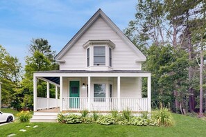 Ein weißes, zweistöckiges Haus mit Veranda, einer grünen Tür und einem kleinen Fenster darüber.