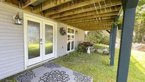 A covered porch with a wooden ceiling, a white door with glass panels, and a decorative rug. - Slice of Heaven, Steps to the Beach (Lincolnville)
