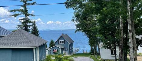 A coastal property with a gravel driveway, a small house, and a larger building with a blue roof.