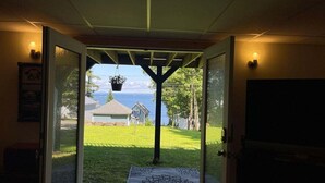 A doorway leading to a grassy yard with a house and a body of water in the background. - Slice of Heaven, Steps to the Beach (Lincolnville)