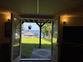 Una puerta que da a un patio con césped, una casa y un cuerpo de agua al fondo.