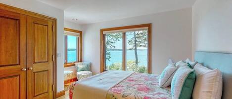 Ein Schlafzimmer mit Bett, einem Fenster mit Meerblick und einer Holztür.