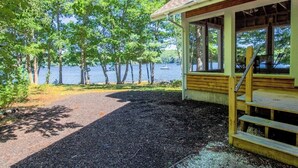 Una baita di legno con veranda che si affaccia su un lago, circondata da alberi.